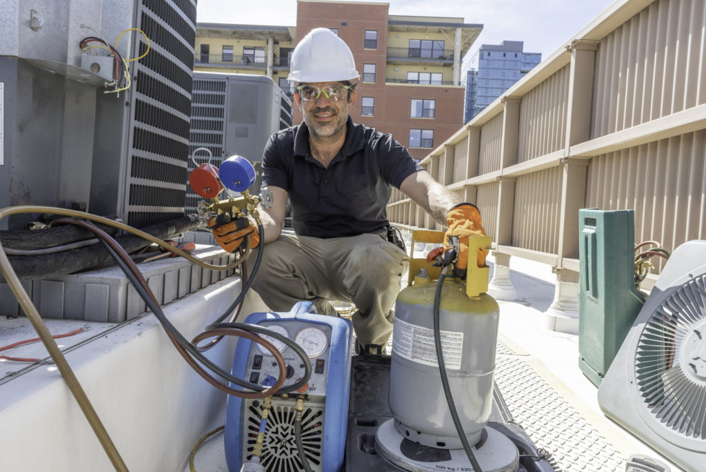 A smiling HVAC technician working with an hvac marketing company recovering refrigerant from a broken air conditioner condensing unit.